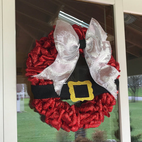 Red Christmas wreath with a silver bow hanging on a glass storm door from a magnetic wreath hanger