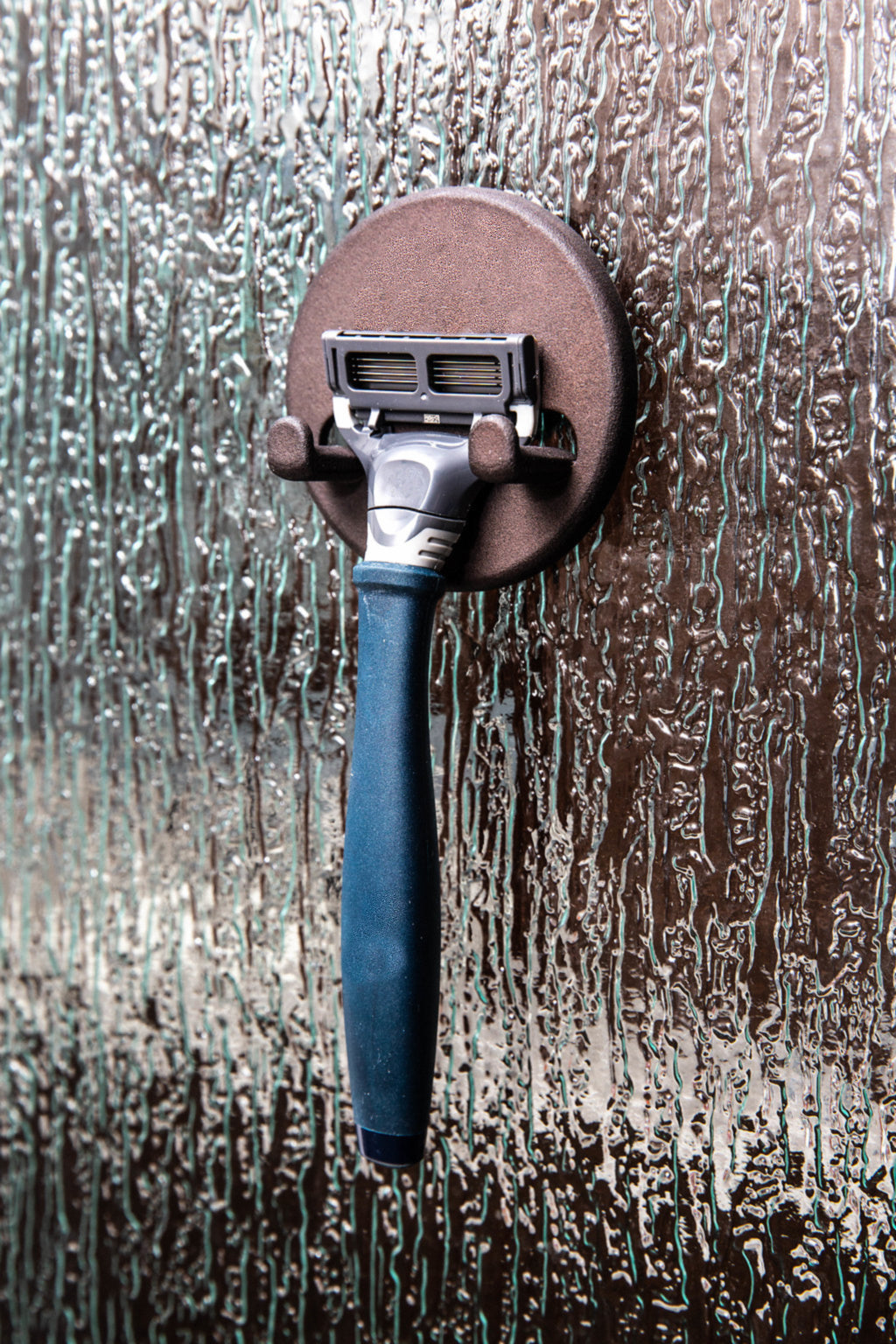 Blue razor hanging from a magnetic shower hook on textured glass