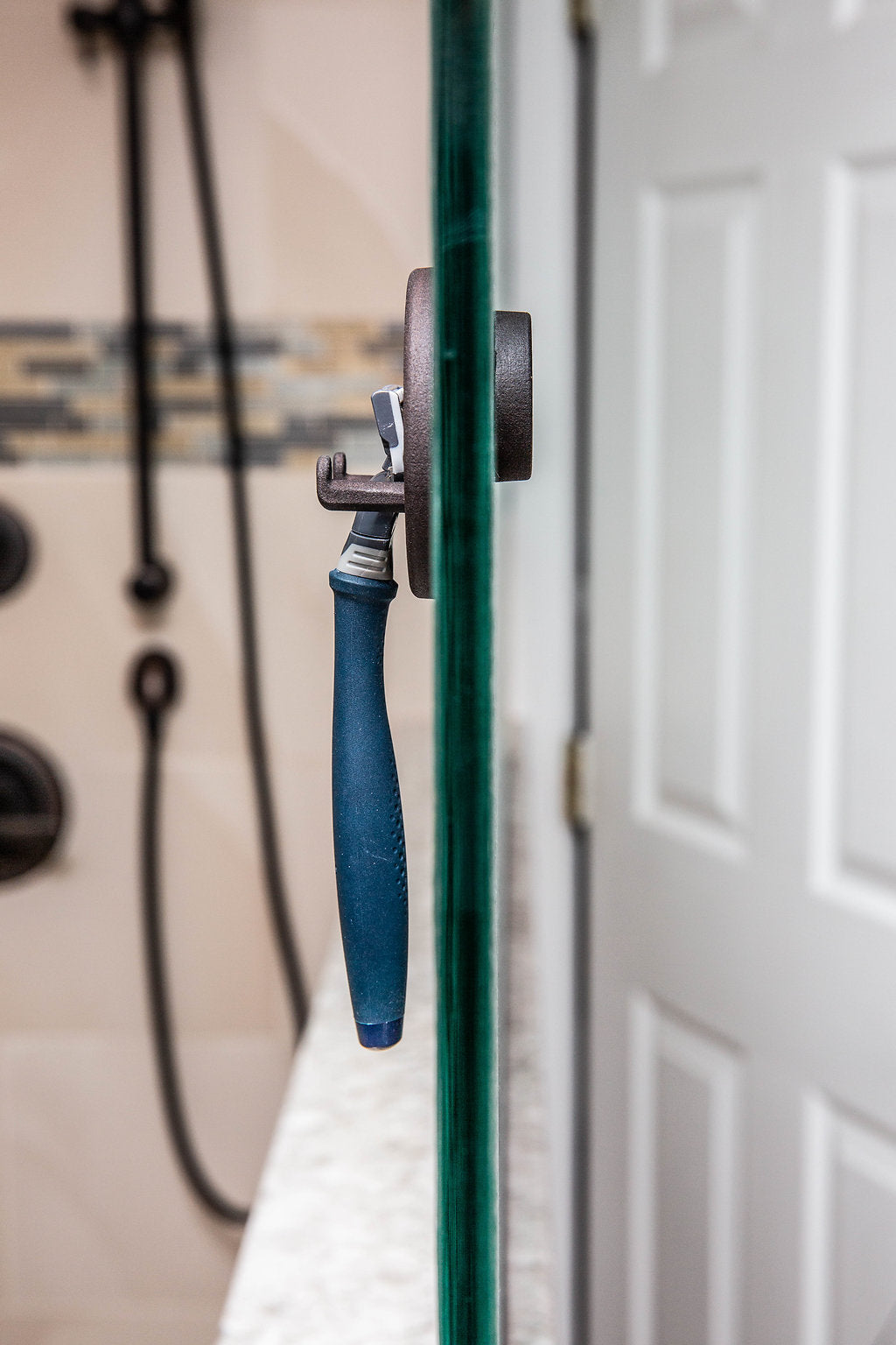 Blue razor on a magnetic holder at the edge of a frameless glass shower door