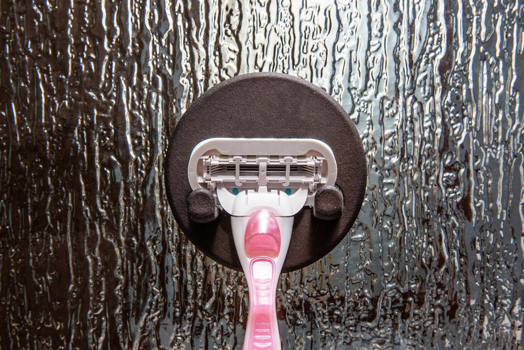 Pink razor held by a round magnetic razor hook on textured shower glass